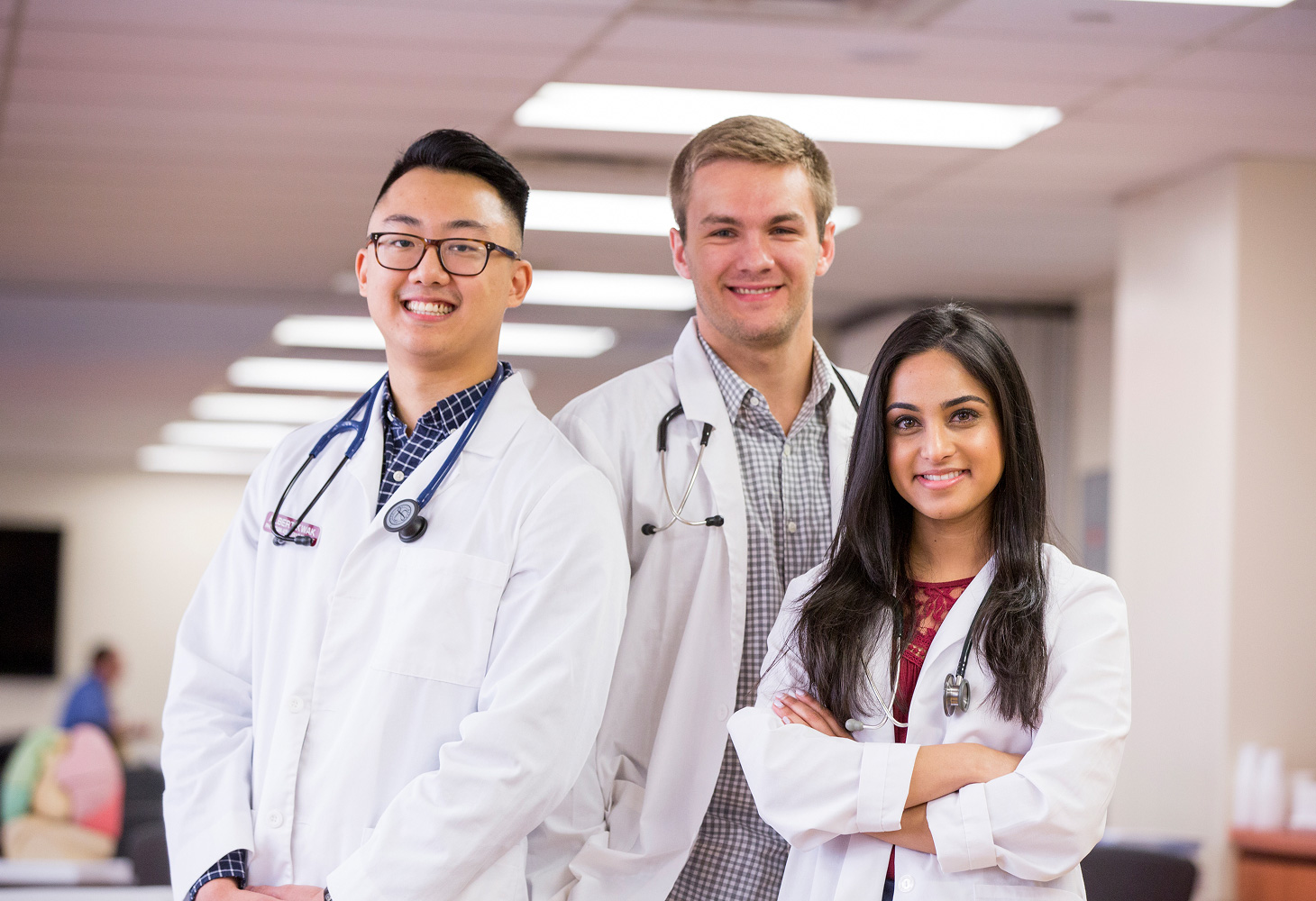 group of three students smiling while wearing white coats.